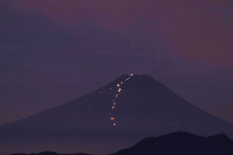 富士山のシルエットに吉田口登山道の光の筋が山頂に向かって延びています。